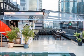A rooftop bar with seating, potted plants, and a view of the city skyline. - Sora Hotel Silom (Bangkok)