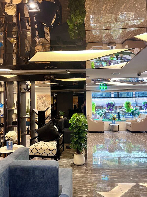 A modern lobby with a seating area, a large digital display, and a potted plant.