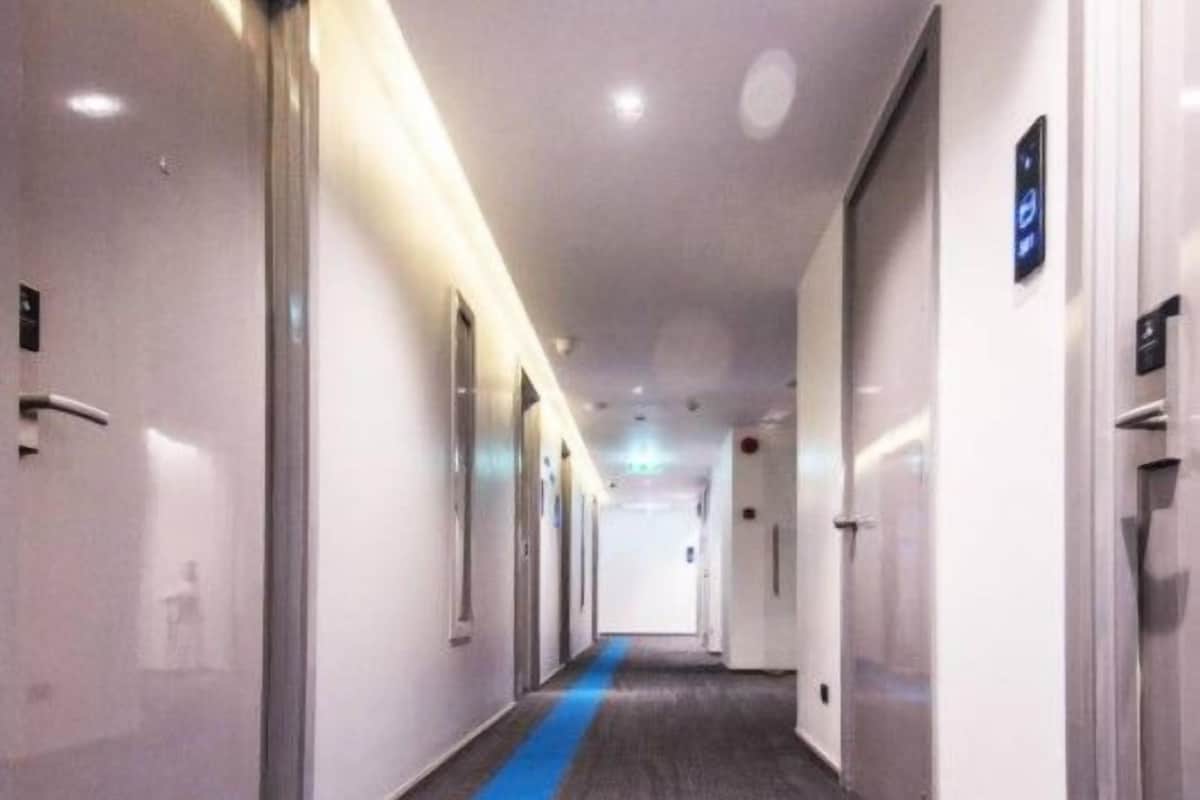 A long, narrow hotel corridor with a blue carpet running down the center, flanked by doors on both sides.