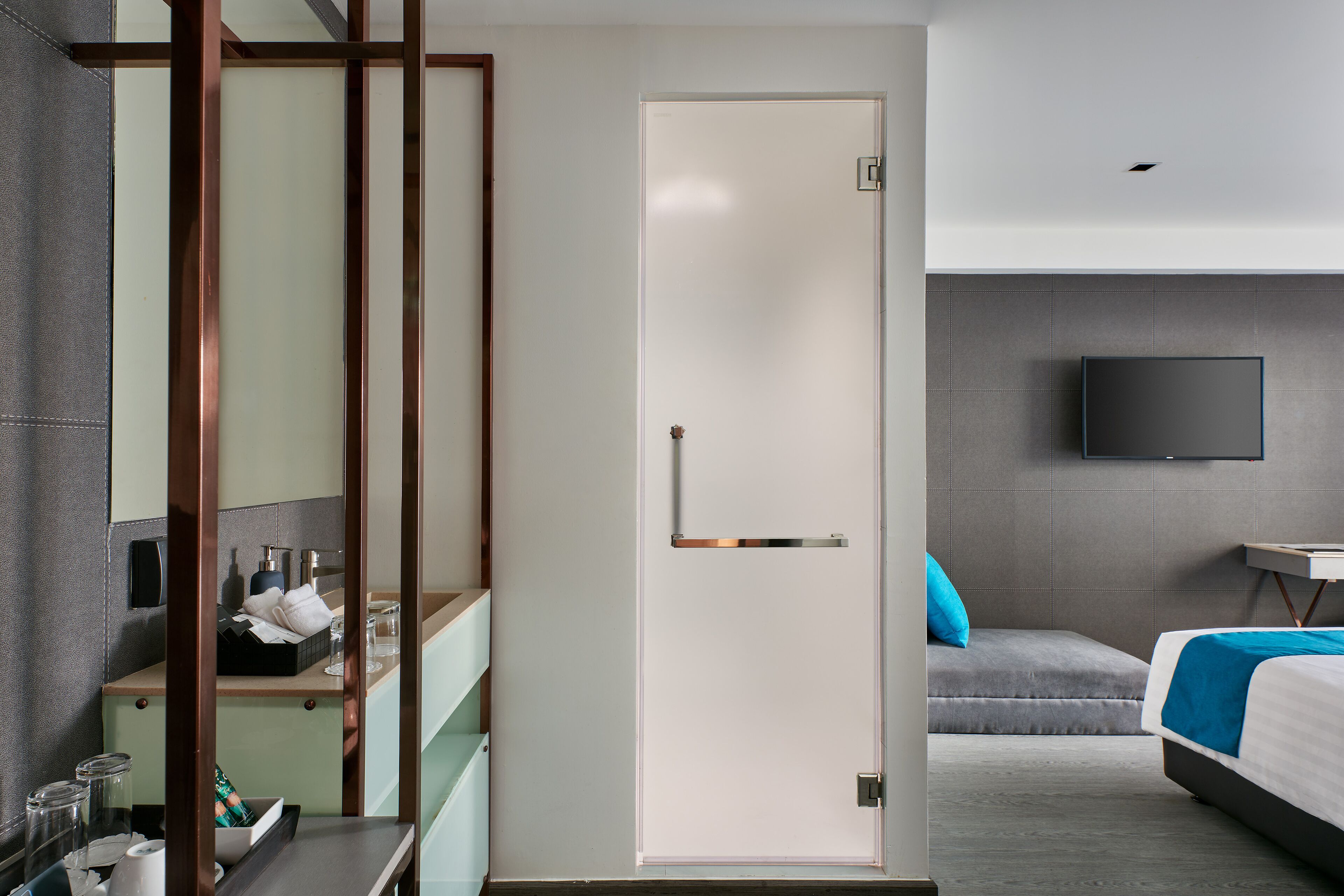 A modern hotel room with a bed, a TV, a desk, and a bathroom area.