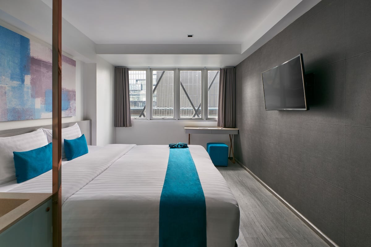 Quarto de hotel com uma cama grande, televisão de tela plana na parede e janela com vista para a cidade.
