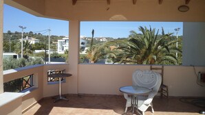 A balcony with a view of a residential area, a small round table, and a wicker chair.