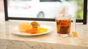 Un plato con un muffin y fruta, y una taza de té sobre una mesa con vistas a un coche blanco a través de una ventana.