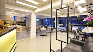 Un moderno vestíbulo de hotel con una recepción, zona de estar y vistas a coches aparcados afuera.