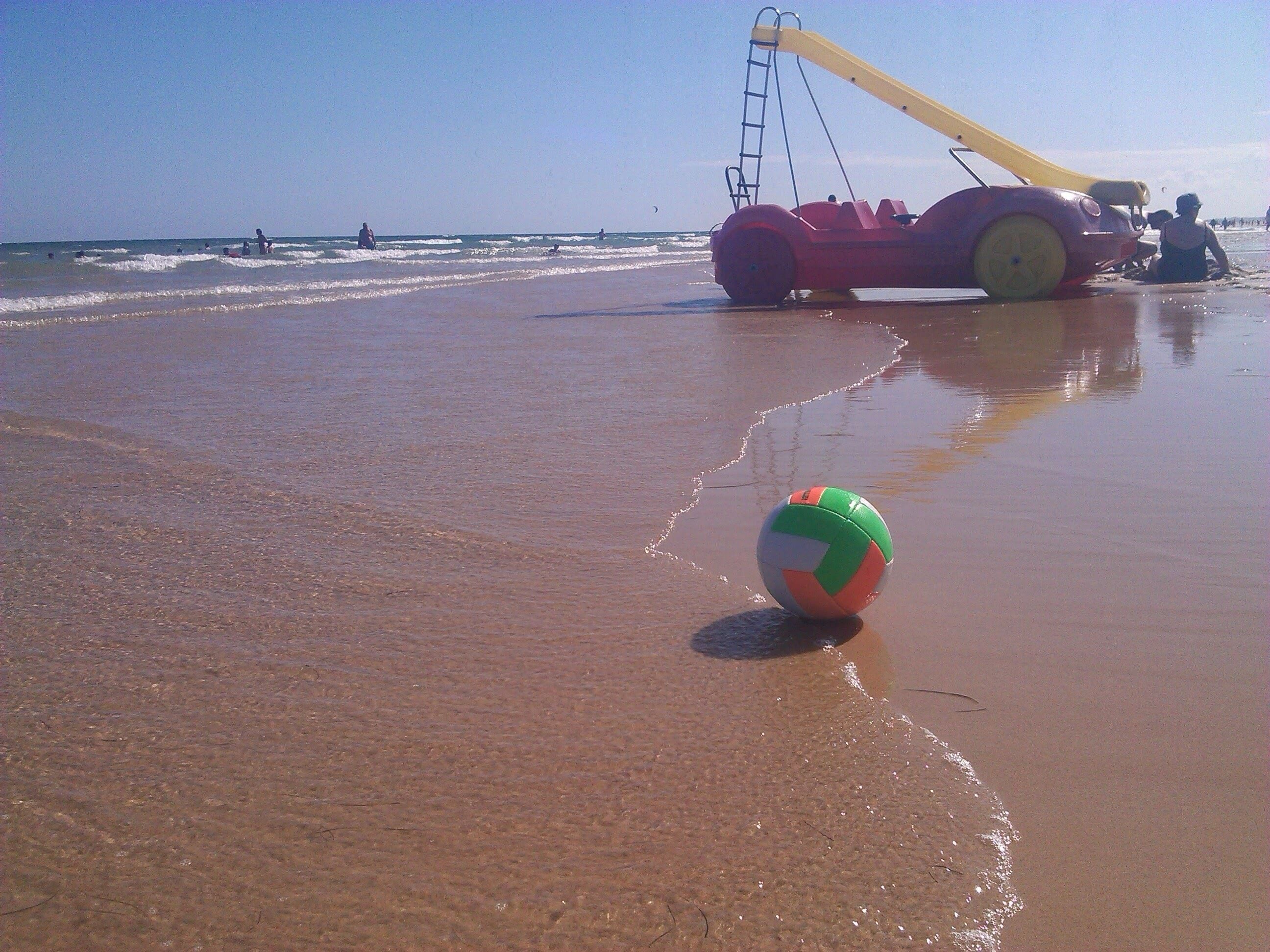 A beach with a volleyball and a large yellow and pink watercraft.