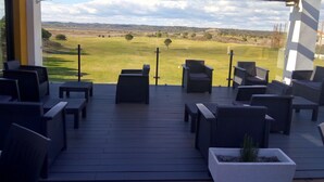Ett takförsett utomhusområde med sittplatser, möbler av rotting och utsikt över en golfbana.