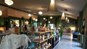 En restauranginteriör med träbord, hängande taklampor och hyllor med ljus och växter.