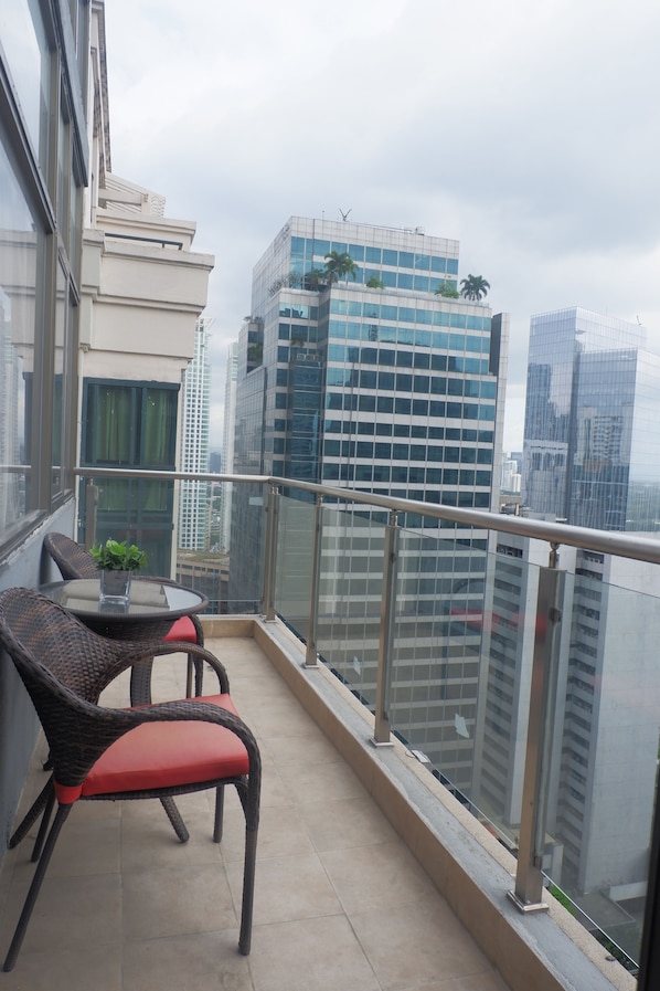 Ein Balkon mit Korbstühlen und einem kleinen Tisch, mit Blick auf eine Stadtlandschaft mit modernen Gebäuden.