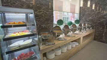 A buffet with various food options, including fruits and dishes in metal containers, set against a marble wall.