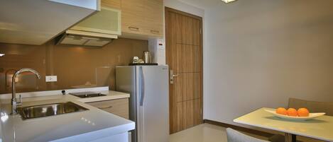 Una cocina moderna con un lavamanos de acero inoxidable, un refrigerador y un mueble de madera. Hay una mesa con un plato de naranjas y una silla.