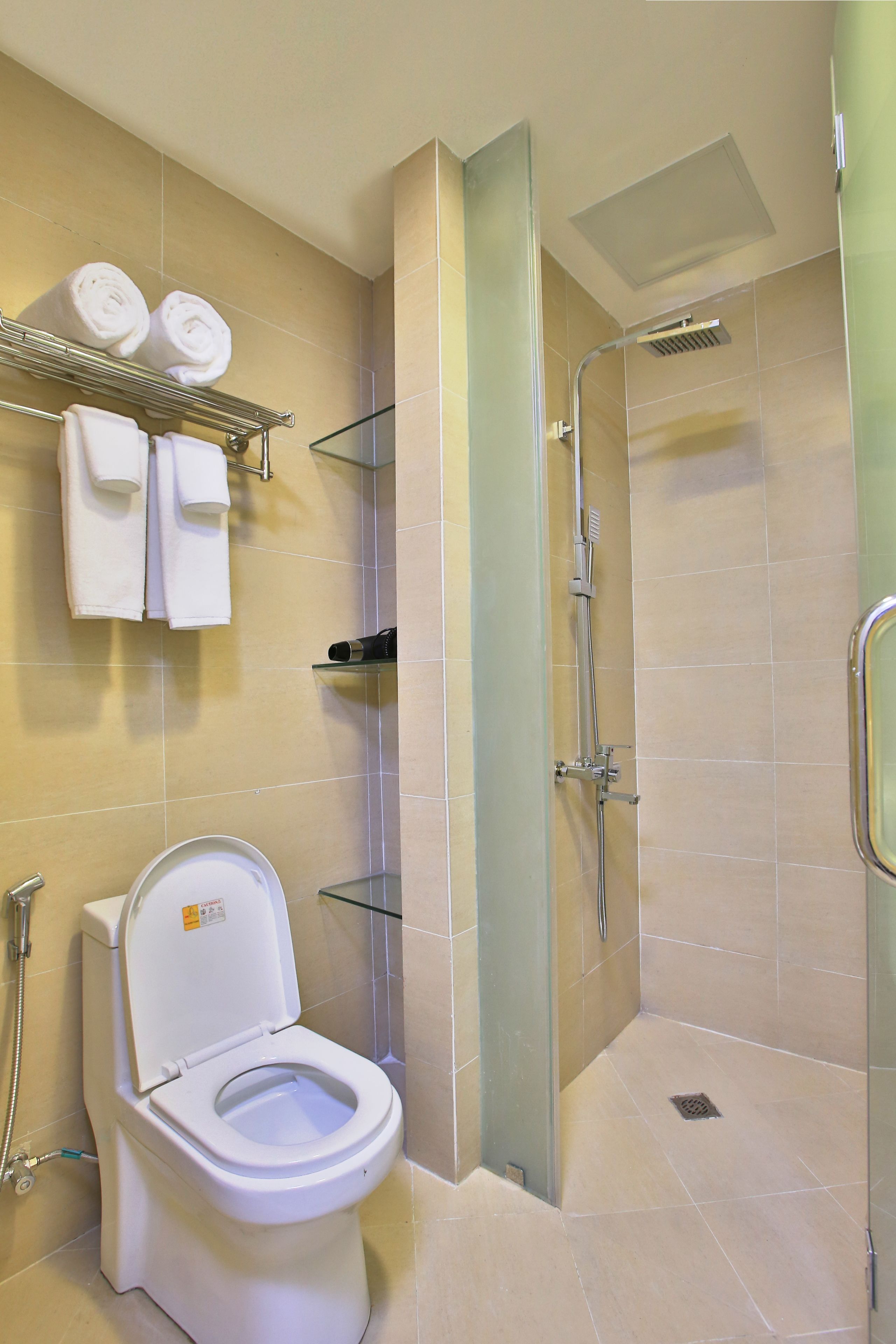 A modern bathroom with a toilet, a glass shower enclosure, and a towel rack with towels.