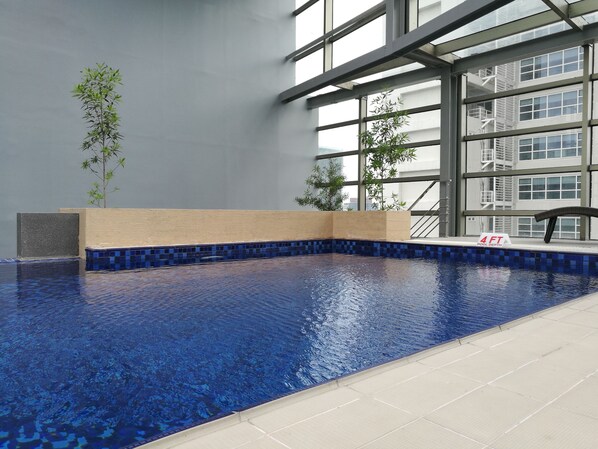 An indoor swimming pool with a 4 ft depth sign, surrounded by large windows and indoor plants.