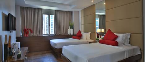 A hotel room with two beds, a TV, a large mirror, and a window with curtains.