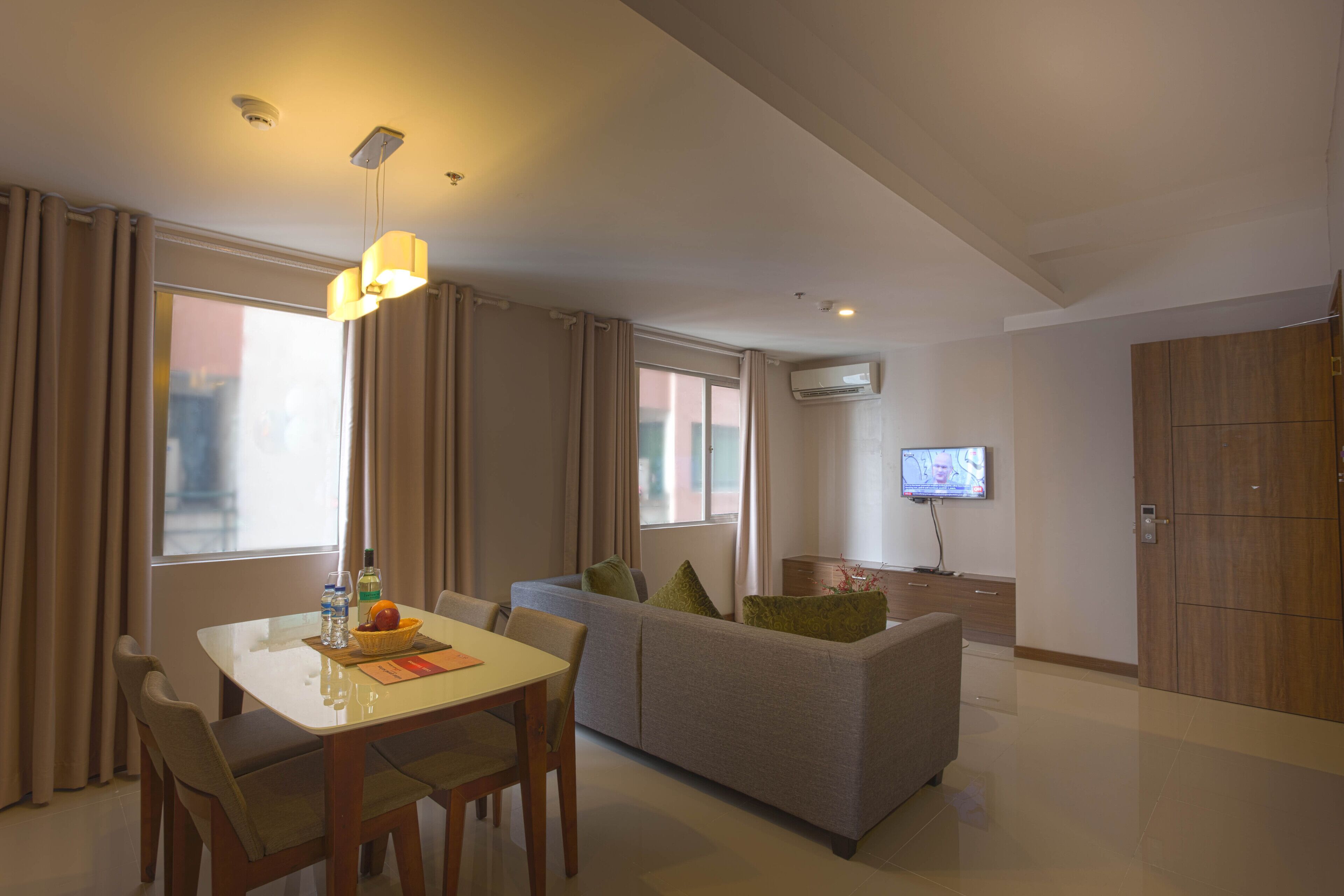 A modern hotel room with a dining area, sofa, TV, and an air conditioning unit.