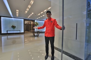 Eine Hotelhalle mit modernem Design, inklusive Glastrennwand, einer Rezeption und einer Zierpflanze.