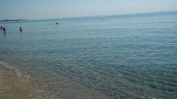 A beach with clear shallow water, a sandy shore, and distant landforms.