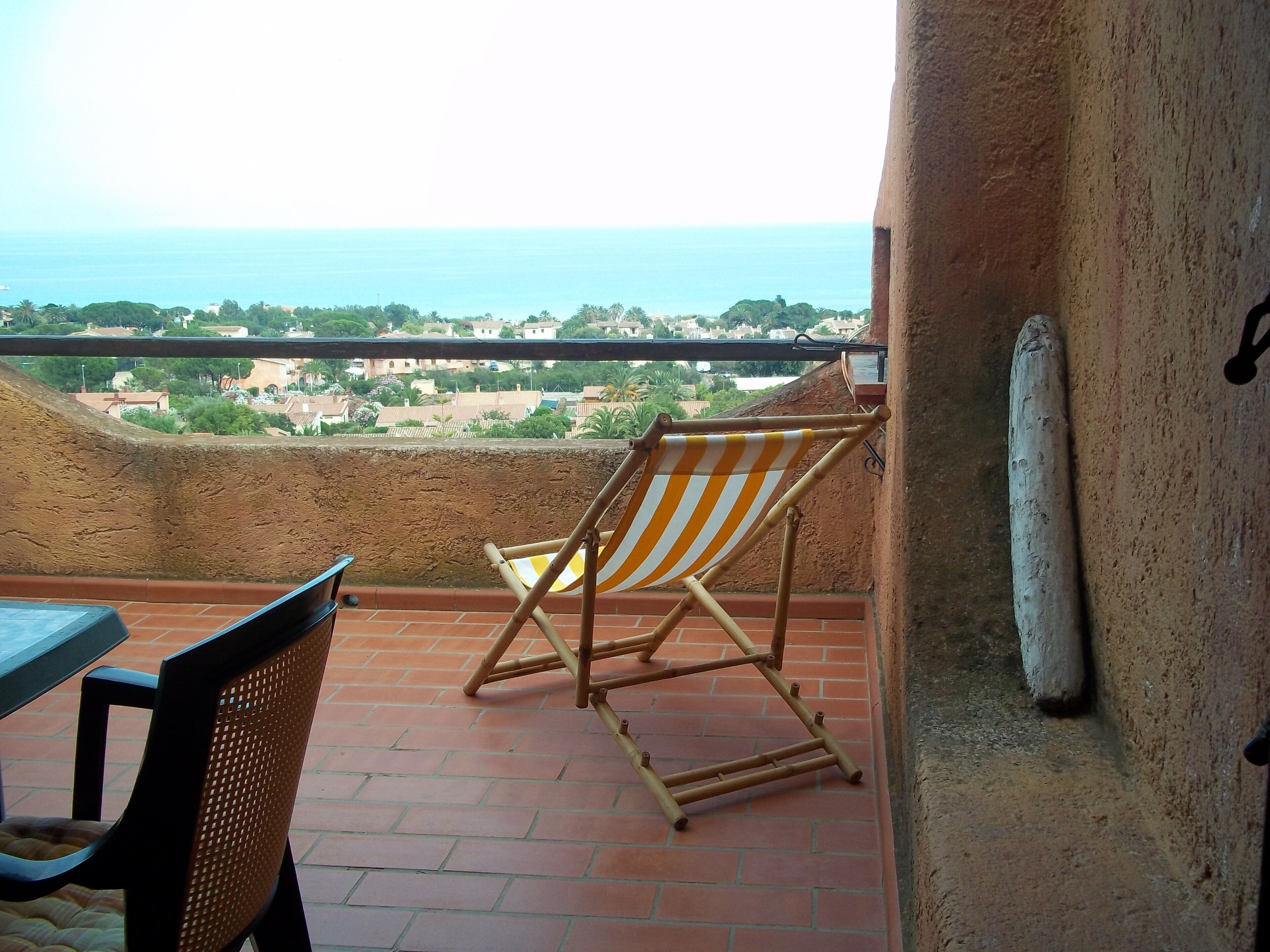A balcony with a view of the sea, a striped beach chair, and a table.