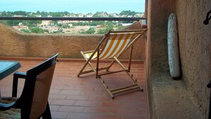 A balcony with a view of the sea, a striped beach chair, and a table.