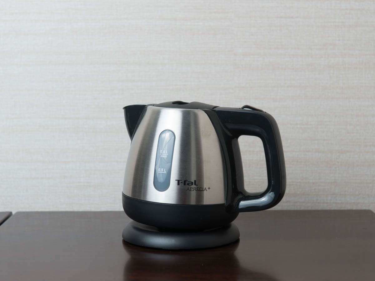 Una tetera eléctrica Tefal de acero inoxidable con asa y base negros, sobre una mesa de madera.