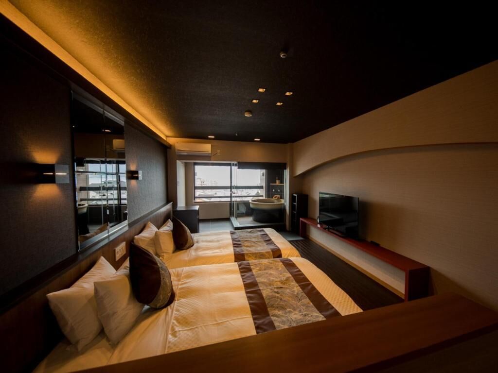 A modern hotel room with a large bed, a TV, and a view of the city through the window.