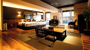 A modern hotel room with a large bed, a dining area with a table and chairs, and a view of the city through large windows. - LiVEMAX RESORT AKIMIYAJIMA (Hatsukaichi)