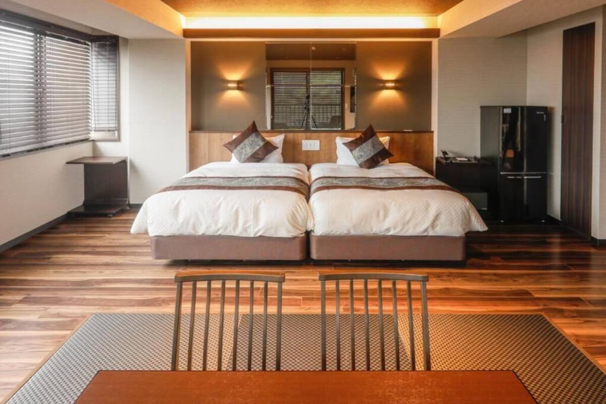 Ein Doppelbett mit zwei Kissen, ein kleiner Tisch und ein Stuhl in einem modernen Zimmer mit Holzboden und einer Deckenleuchte.