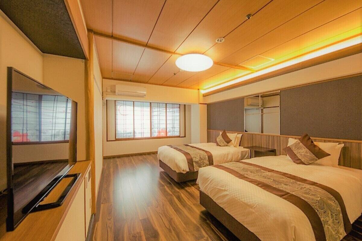 Ein Hotelzimmer mit zwei Betten, einem Flachbildfernseher, Holzböden und einem großen Fenster.