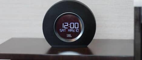 Un reloj digital muestra las 12:00 sobre una mesa de madera oscura frente a una pared lisa.