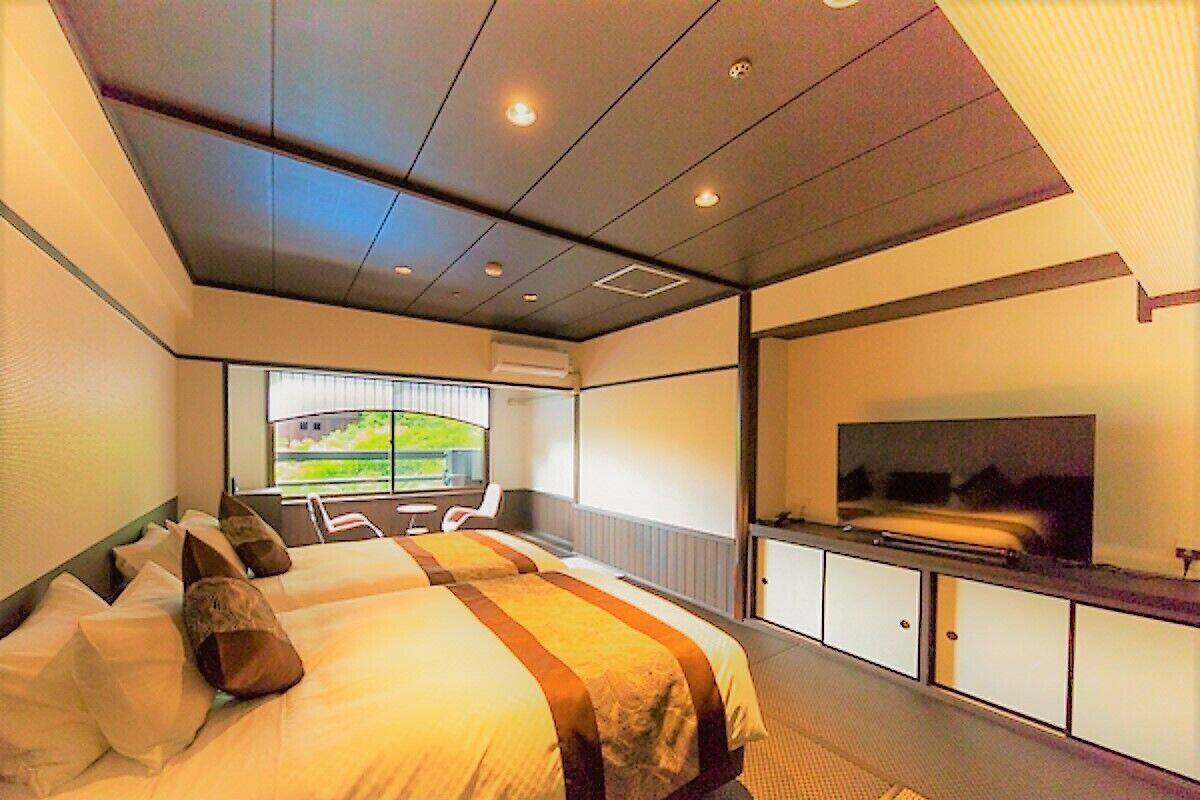 Ein Hotelzimmer mit einem großen Bett, einem Fernseher, einem Schreibtisch und einem Fenster mit Blick auf Grünflächen.