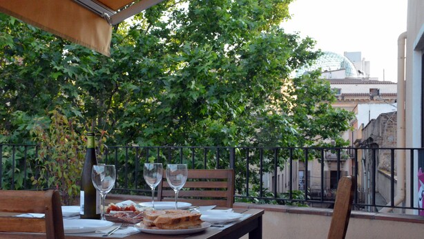 A table set for two with plates, glasses, and a bottle, surrounded by chairs.