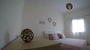 Ein Schlafzimmer mit hölzernem Kopfteil, einem Bett mit rosa Bettdecke, zwei herzförmigen Wanddekorationen und einer Pendelleuchte.