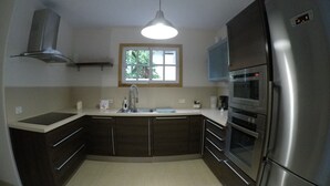 Eine moderne Küche mit einem Edelstahl-Kühlschrank, einem Einbauofen und einer Mikrowelle. Über der Spüle befindet sich ein Fenster, und von der Decke hängt eine Pendelleuchte.