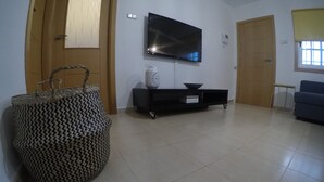 Ein Wohnzimmer mit flachbildfernseher an der Wand, einer schwarzen Unterhaltungseinheit, einem gewebten Korb und einem blauen Sofa.