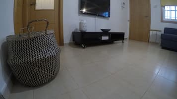 A living room with a flat-screen TV mounted on the wall, a black entertainment unit, a woven basket, and a blue sofa.