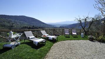 Relax in a serene outdoor space with lounge chairs and a table, surrounded by rolling hills and a distant mountain range.