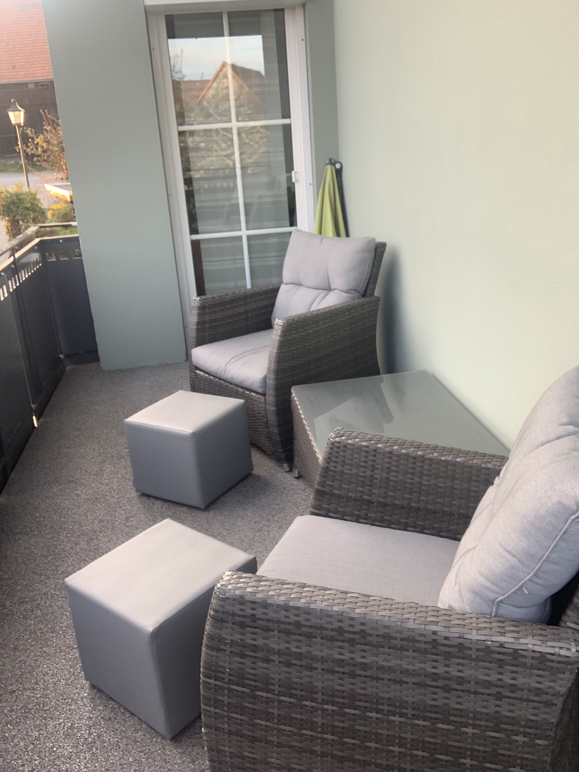 Un balcon agrémenté de meubles en osier, notamment deux fauteuils et deux poufs, ainsi qu’une table en verre.