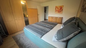 A bedroom with a bed, a nightstand, a wardrobe, and a painting on the wall. - A modern, 80 m² 3-room vacation rental with a balcony. Dogs are welcome. (Goldkronach)