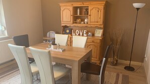 A dining area with a wooden table, white chairs, a cabinet with a 'LOVE' sign, and a floor lamp. - Modern furnished, 80 m² 3-room apartment with south / west-facing balcony (Goldkronach)