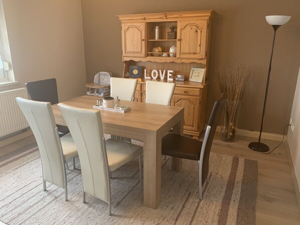 A dining area with a wooden table, four chairs, a cabinet with a 'LOVE' sign, and a floor lamp.