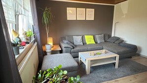 A modern living room with a grey sofa, a wooden coffee table, and a grey rug. There are potted plants on a shelf and a lamp on a side table. - Modern furnished, 80 m² 3-room apartment with south / west-facing balcony (Goldkronach)