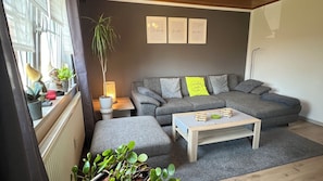 A modern living room with a grey sofa, a wooden coffee table, and a grey rug. There are potted plants on a shelf and a lamp on a side table. - Modern furnished, 80 m² 3-room apartment with south / west-facing balcony (Goldkronach)