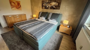 A bedroom with a bed, bedside tables, a nightstand, a dresser, and artwork on the walls. - Modern furnished, 80 m² 3-room apartment with south / west-facing balcony (Goldkronach)