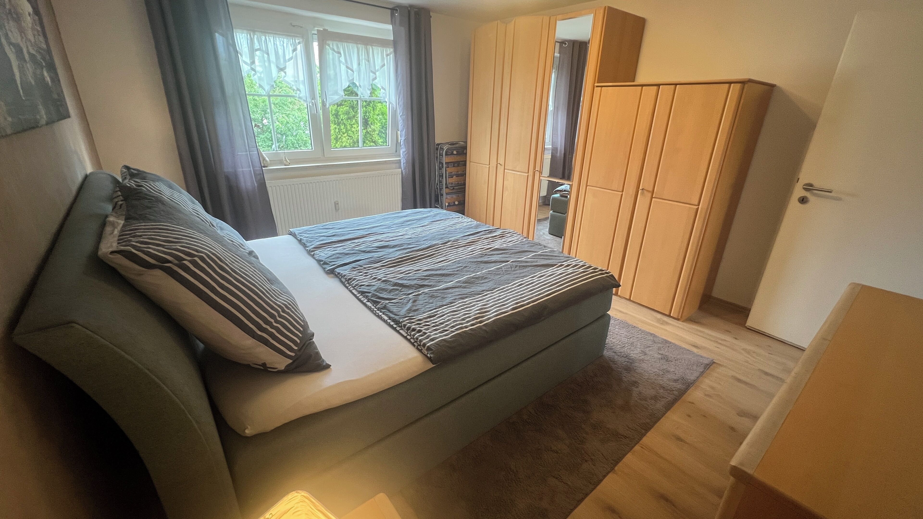 A bedroom with a bed, a wardrobe, a radiator, and a window with curtains.