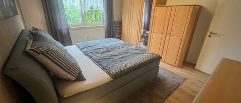 A bedroom with a bed, a wardrobe, a radiator, and a window with curtains.
