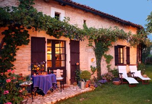 A stone building with a garden patio, outdoor seating, and a table set for dining. - Romantic natural stone cottage in the idyllic natural park Perigord - Limousin (Varaignes)