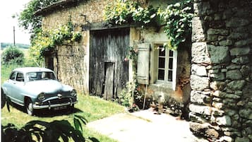Classic car parked in front of a charming stone building with a large door and small window.