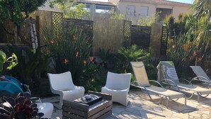 An outdoor patio with white lounge chairs, a wooden coffee table, and a stone floor.