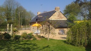 A stone house with a sloped roof and a chimney. There is a small garden with a lawn and a yellow umbrella.