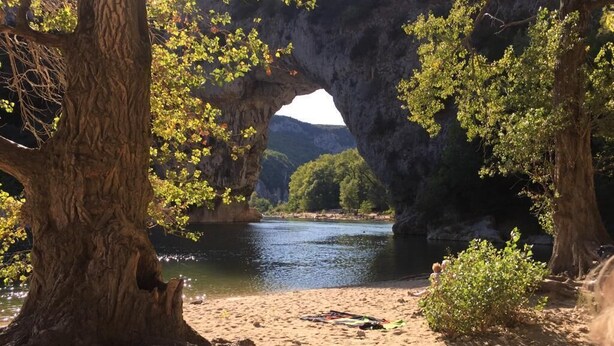 A natural landscape with a large tree in the foreground, a sandy beach, and a body of water under a rock formation. - Spacious villa, private, secure swimming pool Jacuzzi on large, enclosed grounds (Sampzon)