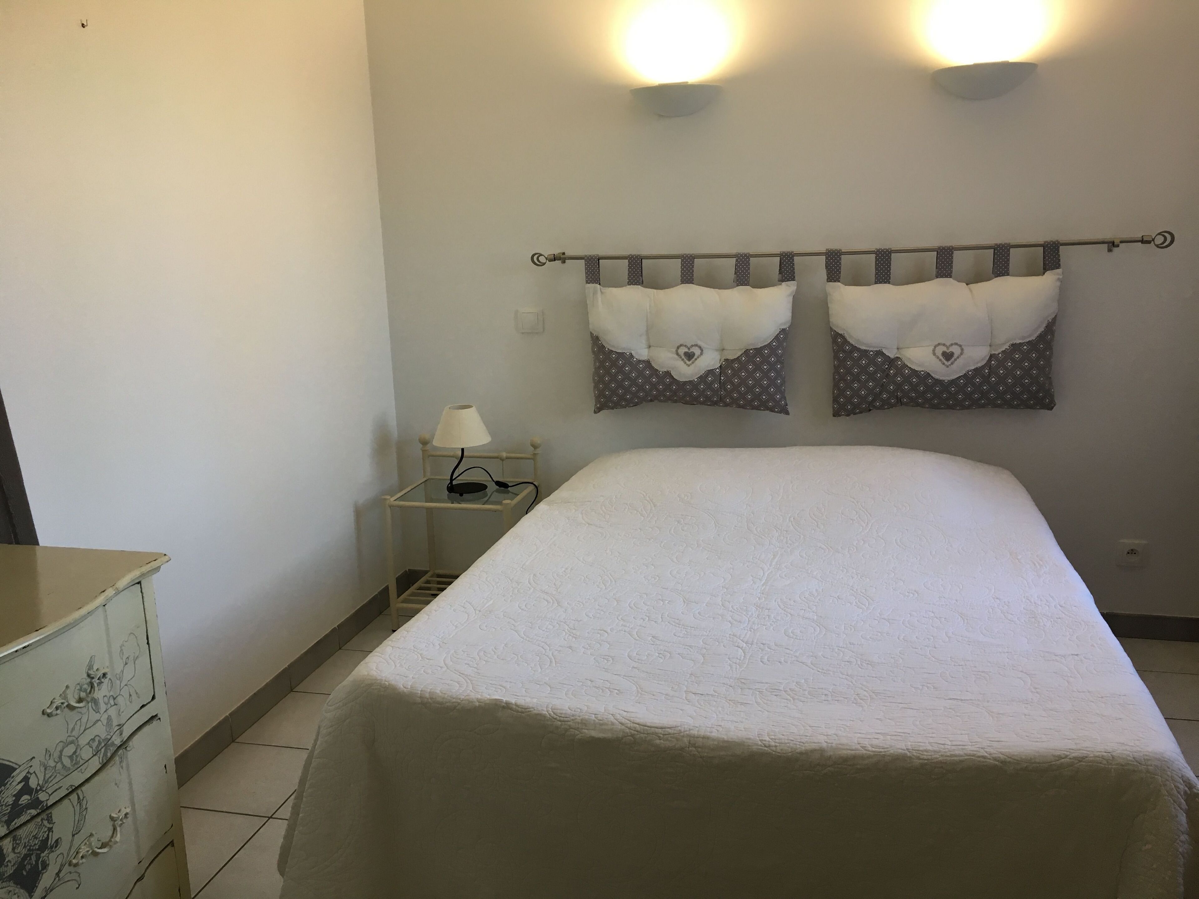 A bedroom with a bed, a nightstand with a lamp, and two wall-mounted light fixtures.